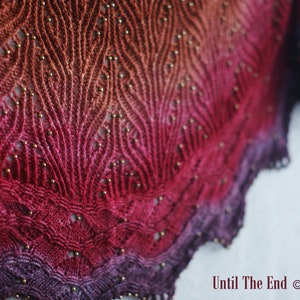 Könnte beinhalten: Nahaufnahme einer rot, lila und orange gestrickten Stola mit goldenen Perlen. Die Stola hat ein Spitzenmuster und ist mit einem gewellten Rand eingefasst. Der Text "Until The End" ist in der unteren rechten Ecke des Bildes sichtbar.