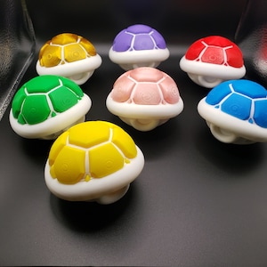 May include: A set of eight colorful turtle shell toys. The shells are made of plastic and have a white base. The shells are in the colors red, blue, green, yellow, pink, purple, gold, and brown.