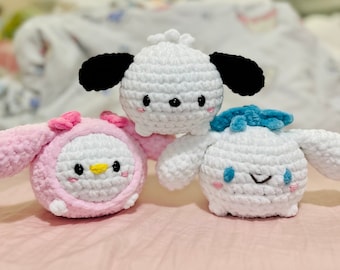 May include: Three crocheted plush toys, each with a different design. The first is a white plush with black ears and a black nose, the second is a pink plush with white ears and a yellow beak, and the third is a white plush with blue ears and a blue nose.