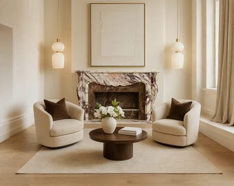 Puede incluir: Un salón con dos sillones crema con cojines marrones, dispuestos alrededor de una mesa de centro redonda marrón oscuro. Una chimenea de mármol y una gran obra de arte enmarcada son centrales. Dos lámparas colgantes cuelgan del techo.