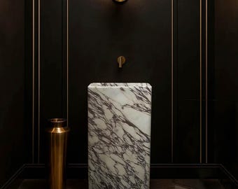 May include: A modern bathroom with a marble sink and gold fixtures. The sink is a rectangular block with gray and white veining. A gold faucet and a matching sconce with a round light are mounted on the black wall. A gold vase sits on the floor.