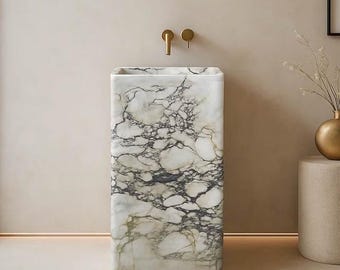 May include: A rectangular marble pedestal sink with a white and gray veined pattern. The sink has a square basin and is mounted below a gold faucet. The bathroom fixture is set against a neutral wall.