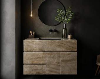 May include: A contemporary bathroom vanity with a marble effect, featuring a black sink and tap. A round black mirror hangs above, with a green plant in a glass bottle. A single light fitting hangs from the ceiling.