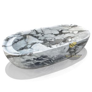 May include: Oval-shaped marble bathtub with a gray and white veined pattern. The tub has a smooth, polished finish and a curved interior. The design includes a built-in headrest. The product is from MarbleBee.