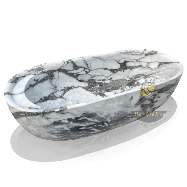 May include: Oval-shaped marble bathtub with a gray and white veined pattern. The tub has a smooth, polished finish and a curved interior. The design includes a built-in headrest. The product is from MarbleBee.