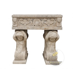 Puede incluir: Banco de piedra beige con intrincadas tallas. La parte superior rectangular tiene un borde en forma de cuerda y tallas de hojas, sostenida por dos figuras arrodilladas. Ideal para jardines o espacios exteriores.
