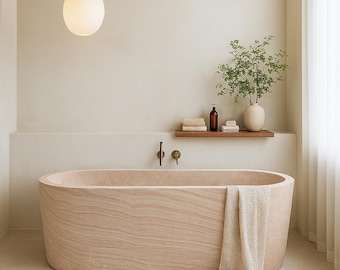 May include: A beige stone bathtub with a matching towel draped over the side. A wooden shelf holds towels, a bottle, and a vase with greenery. A pendant light hangs above the tub, and the walls are a neutral color.