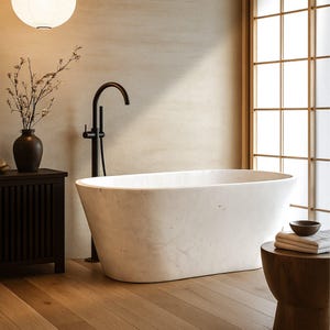 May include: A modern bathroom featuring a white marble bathtub with a black faucet. A dark wooden cabinet holds a vase of flowers. The room has a minimalist design with a paper lantern and wooden floors.
