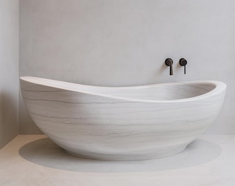 May include: A large, white marble bathtub with a unique, curved design. The tub has a smooth, polished finish and sits on a light-colored tiled floor. Two black faucet handles are mounted on the wall above the tub. The bathroom has a minimalist design.