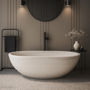 May include: A modern bathroom interior featuring a large, oval-shaped, light-colored bathtub. The bathroom has a minimalist design with a black towel rack, a round mirror, and a small side table with a vase and candle. The walls are a neutral color.