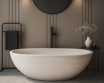 May include: A modern bathroom interior featuring a large, oval-shaped, light-colored bathtub. The bathroom has a minimalist design with a black towel rack, a round mirror, and a small side table with a vase and candle. The walls are a neutral color.