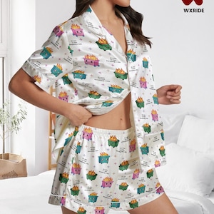 May include: White satin pyjama set featuring a repeating pattern of cartoon dumpsters on fire in various colours, with the text "It's fine, everything's fine." The set includes a button-down shirt and shorts.