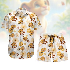 Puede incluir: Una camisa blanca de botones y pantalones cortos a juego con un patrón repetido de cachorros de león y flores. La camisa tiene cuello y mangas cortas. Los pantalones cortos tienen cintura elástica y cordón.