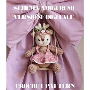 Può includere: Una bambola amigurumi a uncinetto a forma di cervo con un vestito rosa, appesa a un'altalena di legno. La bambola ha una corona floreale ed è ambientata su uno sfondo rosa. Il testo sull'immagine recita "SCHEMA AMIGURUMI VERSIONE DIGITALE CROCHET PATTERN."