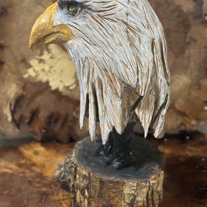 May include: A hand-carved wooden sculpture of a bald eagle with a white head and yellow beak. The eagle is perched on a wooden base.