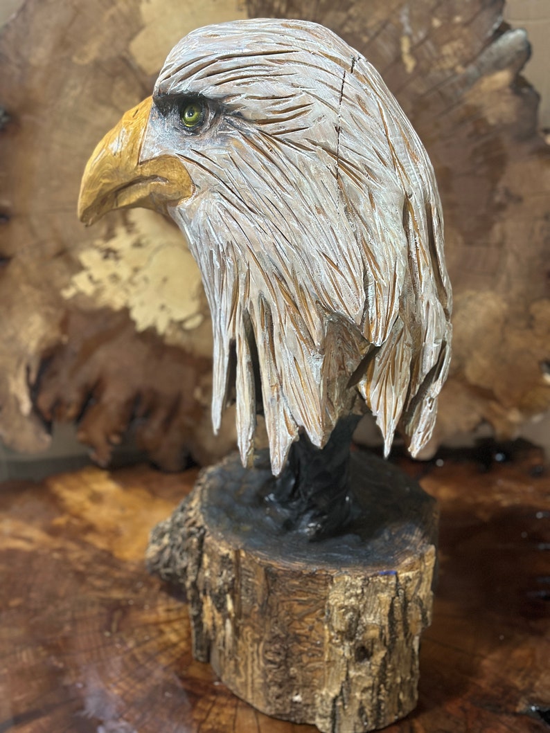 May include: A hand-carved wooden sculpture of a bald eagle with a white head and yellow beak. The eagle is perched on a wooden base.