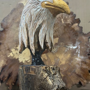May include: A hand-carved wooden sculpture of a bald eagle with a detailed head and feathers. The eagle is perched on a wooden base.