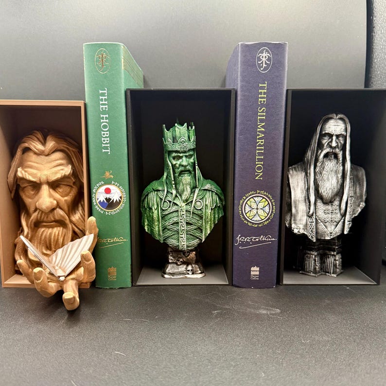 May include: A collection of fantasy-themed bookends featuring busts of characters and two books. The bookends include a brown bust holding a butterfly, a green bust with a crown, and a silver bust with a long beard. The books are green and purple.