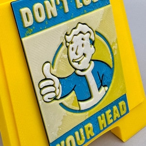 May include: A yellow sign with a blue and cream-colored rectangular emblem. The emblem features a cartoon character giving a thumbs up, with the text "DON'T LOSE YOUR HEAD".