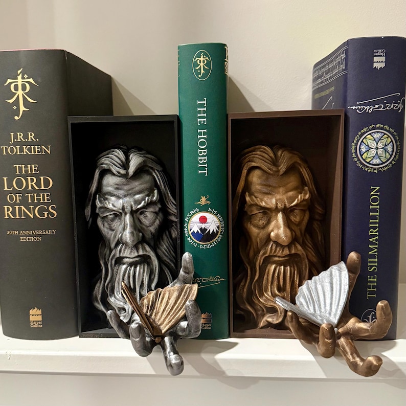 May include: Two bookends featuring Gandalf from Lord of the Rings. One is silver, the other is bronze. Each bookend has a box frame and holds a butterfly. Books from the series are in the background.