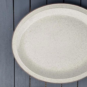 May include: A large, oval, white ceramic serving platter with a speckled finish and a brown rim.
