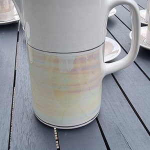 May include: White ceramic teapot with a lid and a handle. The teapot has a gold band around the middle and a iridescent glaze on the bottom half.