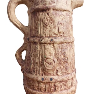 Peut inclure: Un pichet en céramique brun en forme de tonneau en bois avec une anse. Le pichet a une surface rustique et texturée et est décoré d'accents noirs.