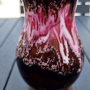 Puede incluir: Un jarrón de cerámica marrón con un diseño marmoleado rosa y blanco. El jarrón tiene una boca ancha y una base redondeada.
