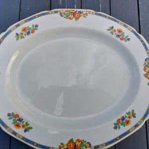 Puede incluir: Una fuente ovalada blanca con un diseño floral azul y dorado. La fuente tiene dos asas y es perfecta para servir comida.