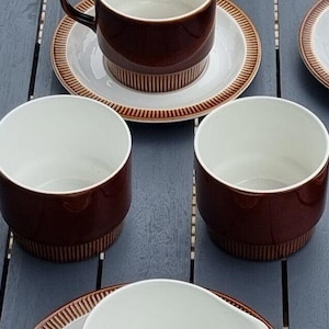 Puede incluir: Juego de tazas y platillos de té de cerámica marrón y blanca. Las tazas tienen una banda marrón alrededor de la parte superior y un interior blanco. Los platillos tienen una banda marrón alrededor del borde y un centro blanco.