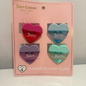 Puede incluir: Un juego de cuatro pinzas magnéticas para chips en forma de corazón en rosa, azul, morado y verde. Cada pinza tiene el logotipo "Juicy". El embalaje es rosa y muestra el logotipo "Juicy Couture" y las palabras "Magnetic Chip Clips".