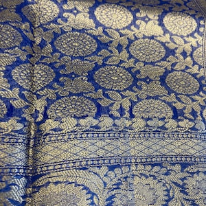 Könnte beinhalten: Ein leuchtend königsblauer Stoff mit einem komplizierten Webmuster aus goldenen Blumenmotiven und kreisförmigen Medaillons. Das Textil zeigt eine detaillierte Bordüre mit geometrischen Gittermustern und größeren botanischen Elementen.
