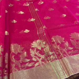May include: A pink sheer saree with gold floral embroidery. The saree has a gold border with a repeating pattern of vertical stripes.