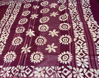 May include: A purple fabric with a white floral pattern. The fabric has a batik design with white flowers and circles on a purple background.