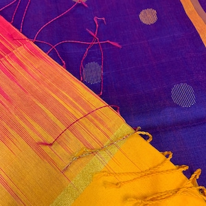 May include: A yellow and orange saree with a pink border and a purple and gold patterned border. The saree has a gold and silver thread border.