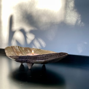 May include: A brown ceramic candle holder with three legs and a textured surface. A small white candle is burning inside the holder.