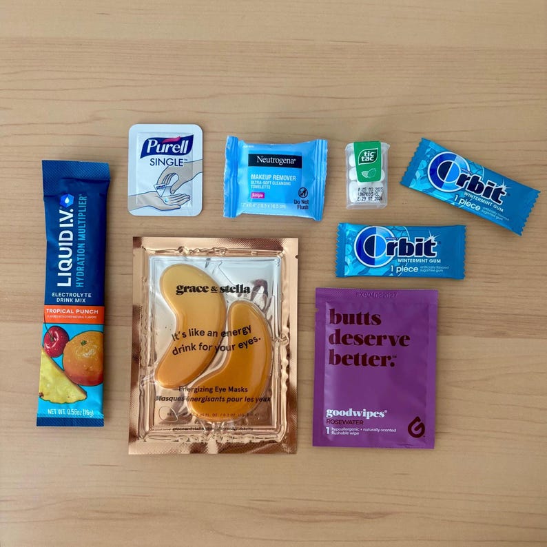 Puede incluir: Surtido de art&iacute;culos de cuidado personal sobre una superficie de madera. Incluye un sobre de mezcla para bebidas Liquid I.V. azul, desinfectante de manos Purell, toallitas desmaquillantes Neutrogena, caramelos de menta Tic Tac, chicle Orbit, mascarillas para ojos y goodwipes.