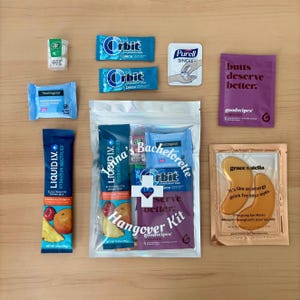 Puede incluir: Una colecci&oacute;n de art&iacute;culos peque&ntilde;os y empaquetados sobre una superficie de madera. Incluye chicles, toallitas desmaquillantes, mezcla para bebidas electrol&iacute;ticas, desinfectante de manos, mascarillas para los ojos y un "Hangover Kit". El kit tiene el texto "Serve Better".