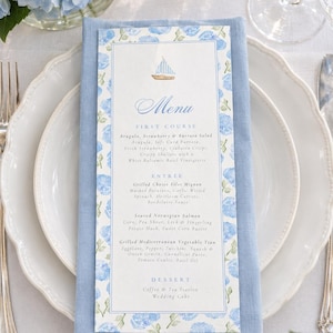 May include: A rectangular paper menu card featuring a watercolor illustration of blue hydrangea flowers and a small sailboat. The text lists a first course, entree, and dessert options, including arugula salad, filet mignon, salmon, and vegetable tian.