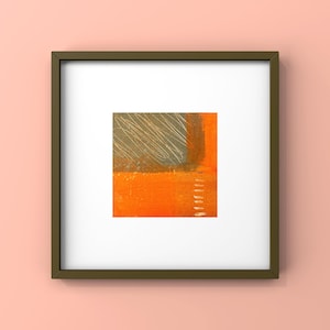 May include: Abstract art print in a dark green frame. The artwork features a square composition with orange and gray blocks, accented by white scribbled lines and a vertical white line. The frame is dark green.