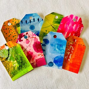 May include: Eight colorful gift tags with abstract watercolor designs. Each tag has a hole punched in the top for string or ribbon.