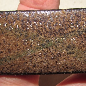 May include: Close-up of a brown leather belt with the text "MADE IN THE USA" and "100% LEATHER" embossed on the surface.