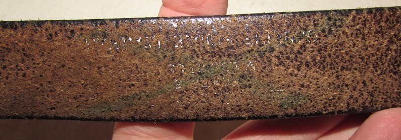 May include: Close-up of a brown leather belt with the text "MADE IN THE USA" and "100% LEATHER" embossed on the surface.