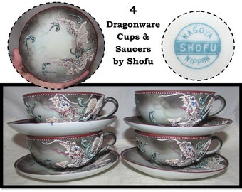 Könnte beinhalten: Set aus vier antiken japanischen Dragonware-Teetassen und Untertassen. Die Tassen und Untertassen haben einen grauen und weißen Hintergrund mit einem silbernen Drachenmuster. Die Untertassen haben einen roten Rand mit weißen Punkten. Die Tassen haben einen roten Rand mit weißen Punkten und ein silbernes Drachenmuster. Die Unterseite der Untertassen trägt einen blauen Stempel mit der Aufschrift "Nagoya Shofu Nippon".