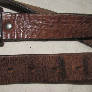 May include: A brown leather belt with a brass buckle. The belt is worn and has a distressed look.