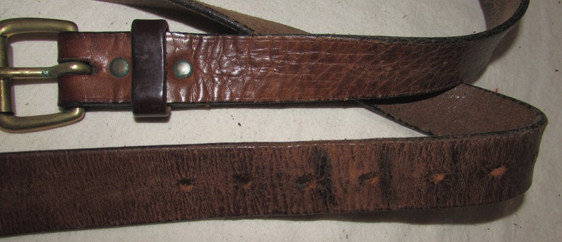 May include: A brown leather belt with a brass buckle. The belt is worn and has a distressed look.