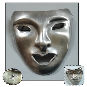 May include: Silver mask brooch with a smiling face and a 925 stamp. The mask is a classic theater design.