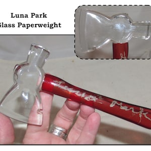 May include: A glass paperweight shaped like an axe with a red handle. The handle has the words "Luna Park" etched into it.