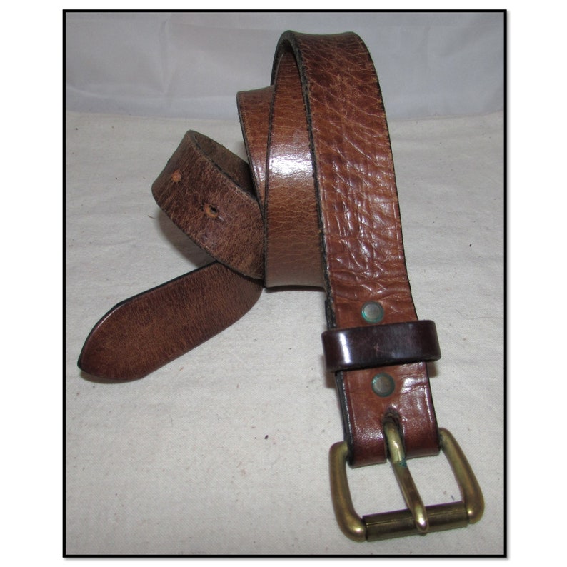 May include: A brown leather belt with a brass buckle. The belt is folded in half and the buckle is visible.