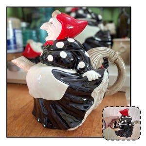 May include: A black and white polka dot teapot shaped like a witch with a red hat and a long, curved spout.